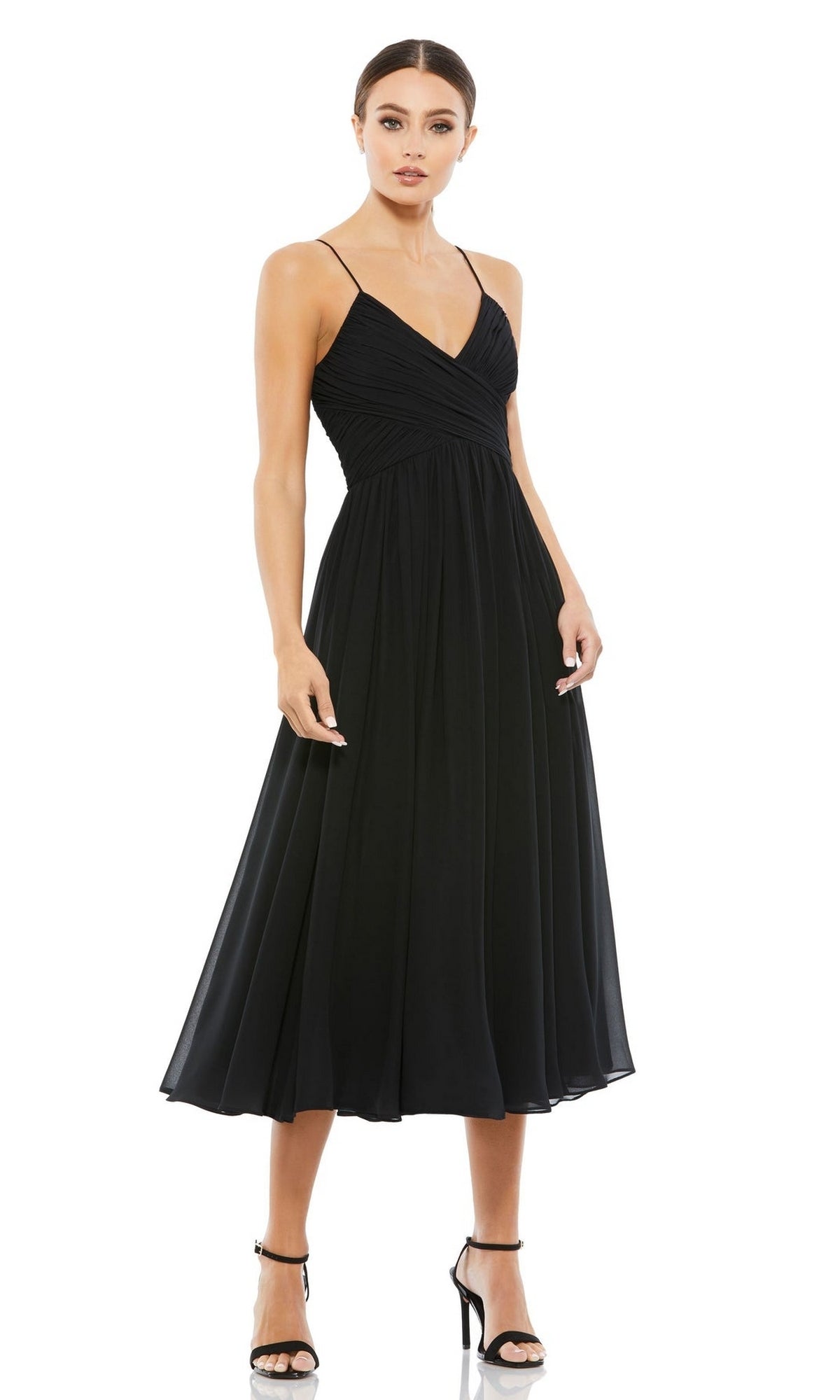 A woman stands against a white background wearing the Mac Duggal 70099 A-Line Midi Wedding Guest Dress, a sleeveless black v-neck dress with thin straps, paired with black high-heeled sandals.